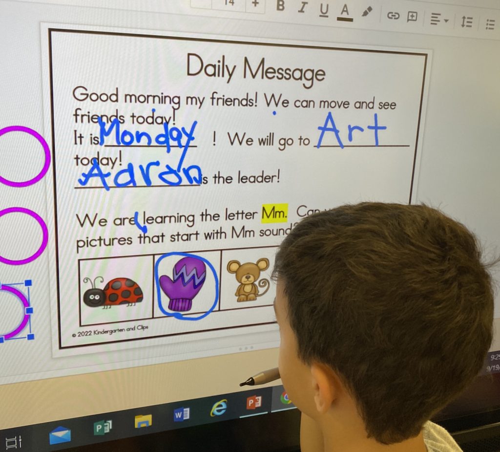 Boy writing on promethean board morning message in kindergarten